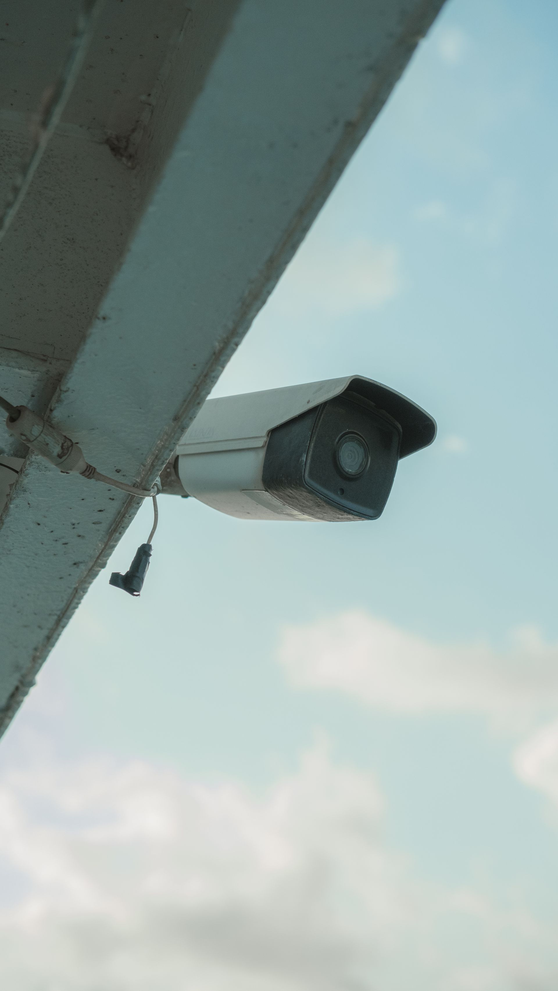 Câmera de CFTV instalada sob a estrutura de um telhado, contra o céu